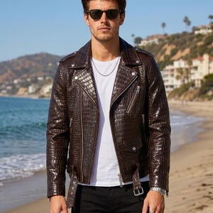 Può includere: Una giacca da moto in pelle marrone scuro con un motivo testurizzato a stampa coccodrillo, caratterizzata da un ampio colletto dentellato, cerniere in metallo color argento, una cintura frontale con fibbia e dettagli con bottoni a pressione.