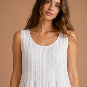 Pode incluir: Um vestido branco sem mangas com decote redondo e riscas verticais. O tecido é adornado com um delicado padrão floral bordado que se repete, criando uma aparência texturizada em toda a peça de vestuário.