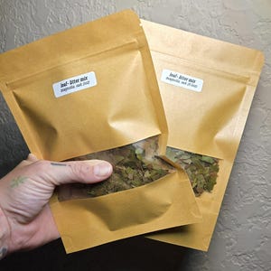 May include: Two tan paper pouches with clear windows containing a leaf-litter mix of magnolia and oak. The front pouch label reads leaf-litter mix magnolia, oak (1oz) and the back pouch label reads leaf-litter mix magnolia, oak (0.5oz).