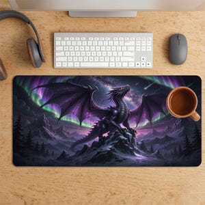 May include: A rectangular desk mat featuring a dark, scaled dragon perched on a snowy mountain peak. The background displays a vibrant purple and green aurora borealis against a starry night sky with silhouettes of pine trees in the foreground.