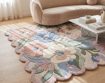 May include: A floral area rug with a scalloped edge. The rug features large, stylized flowers in pastel colors, including pink, blue, and green, set against a cream background. The rug is placed on a wooden floor.