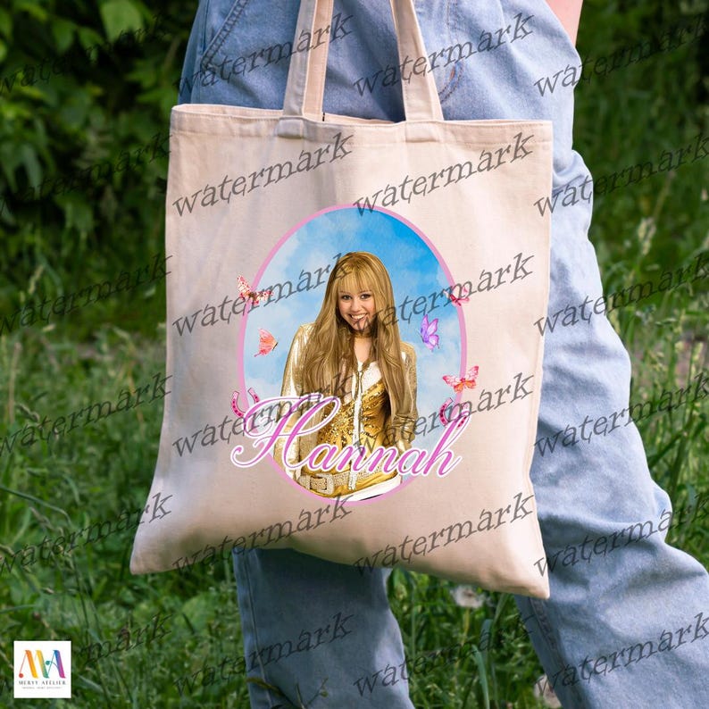 Puede incluir: Bolso tote de lona beige con un dise&ntilde;o circular. El dise&ntilde;o presenta un retrato de una mujer, mariposas y el nombre "Hannah" en escritura rosa sobre un fondo de cielo azul.