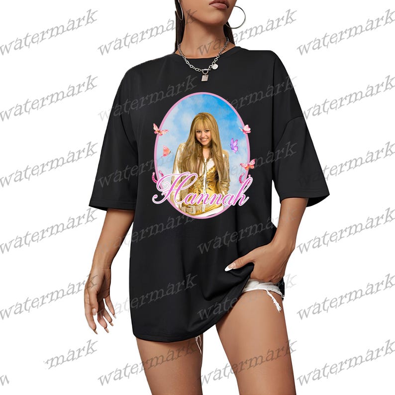 Puede incluir: Camiseta negra de gran tama&ntilde;o con un retrato de una mujer con pelo largo y rubio, enmarcado por un &oacute;valo rosa con mariposas. El nombre "Hannah" est&aacute; escrito en cursiva debajo. La camiseta tiene mangas cortas.