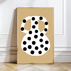 Può includere: Una stampa artistica rettangolare incorniciata raffigurante una forma di vaso bianco con pois neri centrata su uno sfondo beige a tinta unita. Il vaso ha due manici e un corpo arrotondato. Le lettere L.K. sono stampate in bianco nell'angolo in basso a destra.
