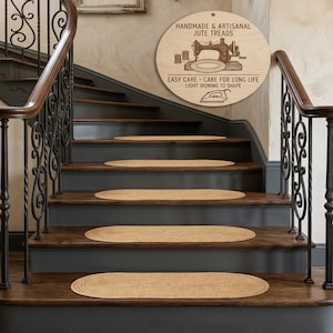 Puede incluir: Peldaños de yute ovalados sobre una escalera de madera. Las huellas son de color beige natural, complementando los escalones de madera oscura y las contrahuellas grises. Un letrero de madera sobre las escaleras dice "HANDMADE & ARTISANAL JUTE TREADS".
