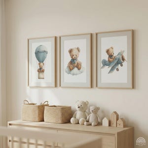 May include: Three framed watercolour prints of teddy bears. One shows a bear in a hot air balloon, another on a cloud, and the third in a biplane. The prints are above a wooden dresser with woven baskets, teddy bears, and wooden houses.