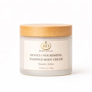 Pu&ograve; includere: Un barattolo di crema corpo montata con coperchio in legno. L'etichetta recita "RO BOTANICALS HONEY+NOURISHING WHIPPED BODY CREAM". Il barattolo contiene 190 g di crema. Su sfondo bianco.