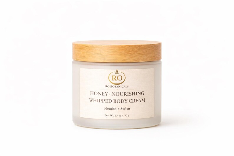 Pu&ograve; includere: Un barattolo di crema corpo montata con coperchio in legno. L'etichetta recita "RO BOTANICALS HONEY+NOURISHING WHIPPED BODY CREAM". Il barattolo contiene 190 g di crema. Su sfondo bianco.