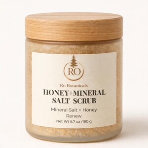 Pu&ograve; includere: Un barattolo di vetro con coperchio in legno contiene uno scrub al miele e sale minerale. L'etichetta recita "HONEY+MINERAL SALT SCRUB" e "Net Wt 190 g". Il barattolo contiene uno scrub marrone chiaro.