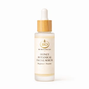 Pu&ograve; includere: Una bottiglia di vetro smerigliato di Honey Botanical Facial Serum con tappo e contagocce in legno. L'etichetta presenta testo dorato e un logo. Il siero &egrave; progettato per illuminare e nutrire la pelle.