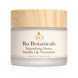 Pu&ograve; includere: Un vasetto di Ro Botanicals Vanilla Lip Treatment. Il vasetto ha un coperchio in legno chiaro e un corpo in vetro smerigliato. L'etichetta recita "Nourishing Honey Vanilla Lip Treatment" e "Natural &bull; Hydrating".