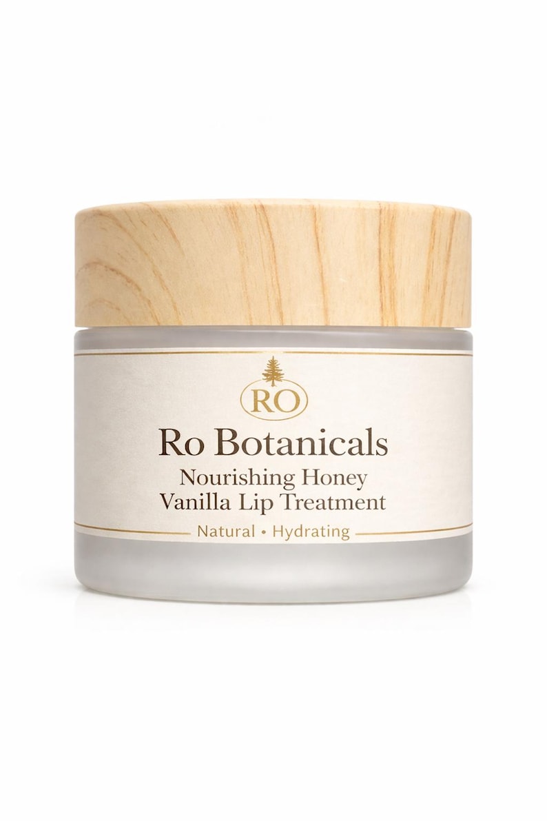 Pu&ograve; includere: Un vasetto di Ro Botanicals Vanilla Lip Treatment. Il vasetto ha un coperchio in legno chiaro e un corpo in vetro smerigliato. L'etichetta recita "Nourishing Honey Vanilla Lip Treatment" e "Natural &bull; Hydrating".
