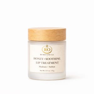 Pu&ograve; includere: Un barattolo di vetro smerigliato con coperchio in legno, etichettato "HONEY + SOOTHING LIP TREATMENT". L'etichetta include anche "RO BOTANICALS" e "Hydrate + Soften". Il barattolo contiene 15g di prodotto.