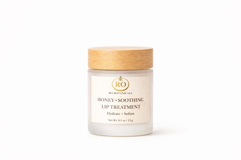 Pu&ograve; includere: Un barattolo di vetro smerigliato con coperchio in legno, etichettato "HONEY + SOOTHING LIP TREATMENT". L'etichetta include anche "RO BOTANICALS" e "Hydrate + Soften". Il barattolo contiene 15g di prodotto.
