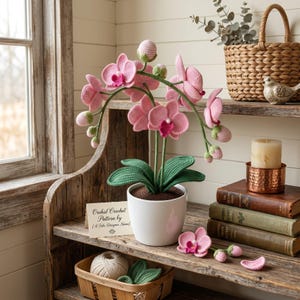 May include: A handcrafted crochet orchid plant with pink flowers, green leaves, and buds in a white pot. The plant sits on a rustic wooden shelf with a small sign that reads "Orchid Crochet Pattern by [A Fake Designer Name]" and other decorative items.