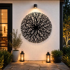 Peut inclure: Une sculpture d'arbre en m&eacute;tal noir, de forme circulaire, est fix&eacute;e sur un mur blanc. Un projecteur l'&eacute;claire. Deux lanternes noires avec des bougies allum&eacute;es bordent l'all&eacute;e, avec des plantes en pot de chaque c&ocirc;t&eacute;.