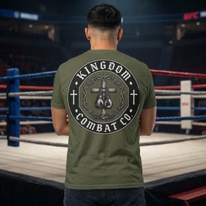 May include: Olive green t-shirt with a circular graphic on the back. The graphic features a cross, boxing gloves, and the text "KINGDOM COMBAT CO." in a black and white design. Two crosses flank the central image.