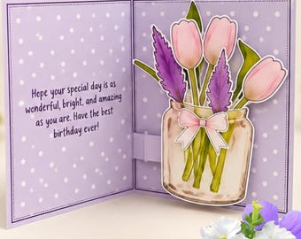 May include: A greeting card with a light purple background featuring white polka dots. The left side displays the text: Hope your special day is as wonderful, bright, and amazing as you are. Have the best birthday ever! The right side shows a mason jar with pink tulips and purple sprigs tied with a light pink bow.