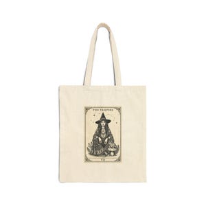 Puede incluir: Bolso tote crema con una ilustración en blanco y negro de una mujer con sombrero de bruja, etiquetado "THE VAMPIRE" con el número romano VII. El diseño incluye estrellas, plantas y una seta.