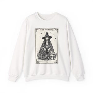 May include: White sweatshirt featuring a tarot card design. The card depicts a woman in a witch hat, labeled "THE VAMPIRE" with the Roman numeral "VII". The illustration is in black and white.