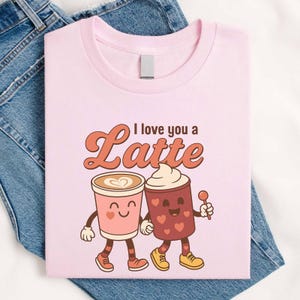 May include: Pale pink t-shirt featuring the text "I love you a Latte" in orange and brown. The graphic shows two cartoon coffee cups holding hands, one with a heart design and the other with whipped cream.