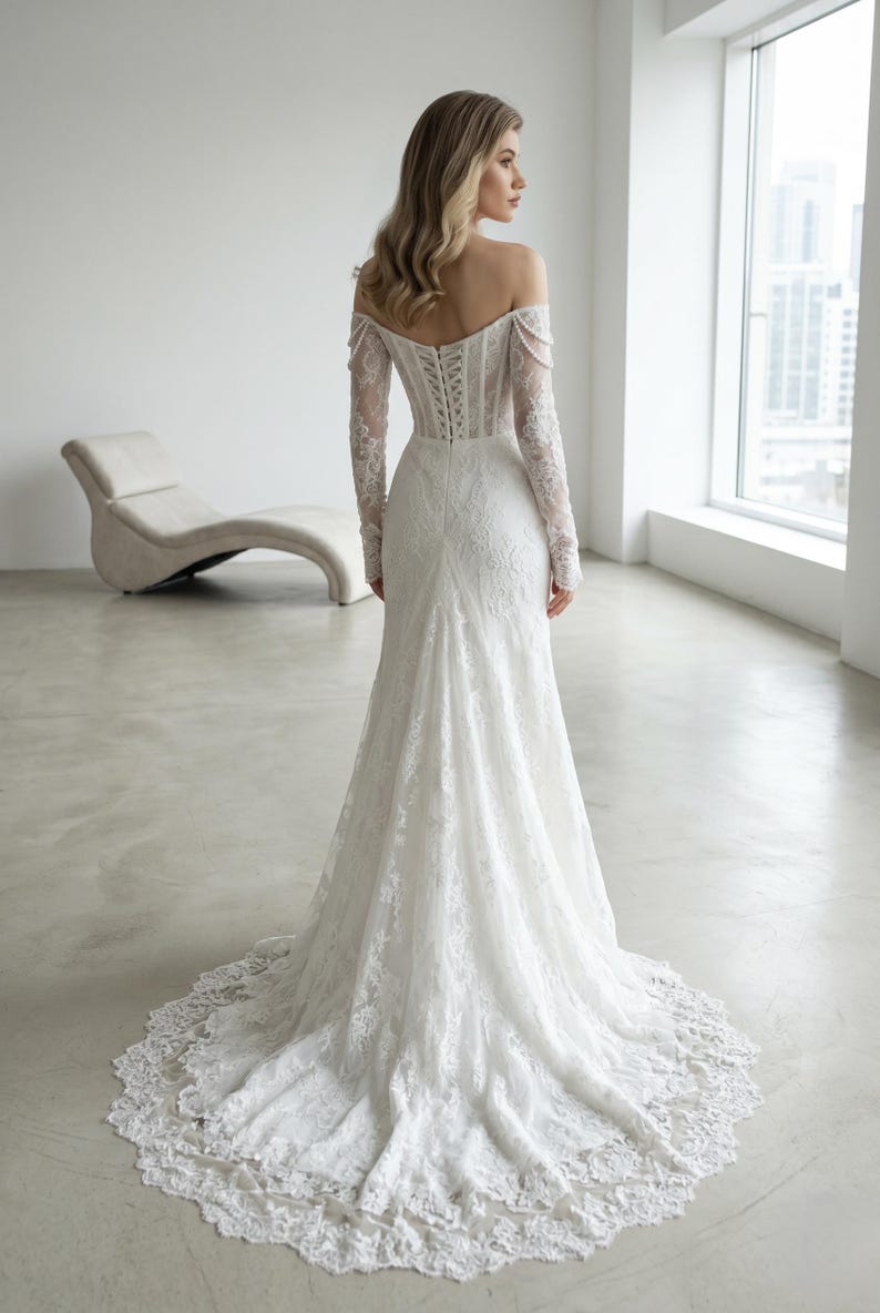 Peut inclure: Une robe de mari&eacute;e blanche en dentelle longue jusqu'au sol avec une encolure d&eacute;gag&eacute;e, des manches longues et un corsage style corset avec un la&ccedil;age au dos. La robe pr&eacute;sente une coupe ajust&eacute;e qui s'&eacute;vase en une tra&icirc;ne &agrave; bordure festonn&eacute;e.