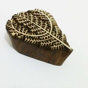 May include: A wooden leaf-shaped block with a detailed, carved leaf pattern. The block is a dark brown color with a lighter, natural wood-colored leaf design. The block is likely used for printing or stamping.