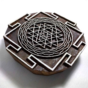 May include: A wooden block printing stamp with a white design of a Sri Yantra, a complex geometric pattern associated with Hinduism and Tantric traditions.