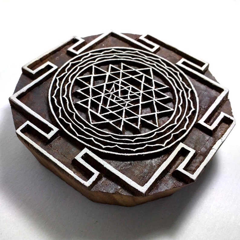 May include: A wooden block printing stamp with a white design of a Sri Yantra, a complex geometric pattern associated with Hinduism and Tantric traditions.
