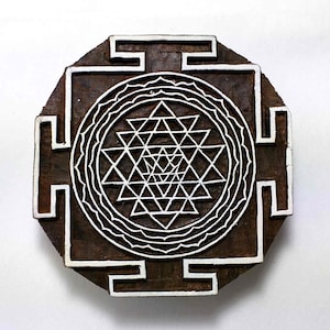May include: A wooden block printing stamp with a white design of a Sri Yantra, a sacred geometric symbol in Hinduism. The design is surrounded by a square frame with a decorative border.