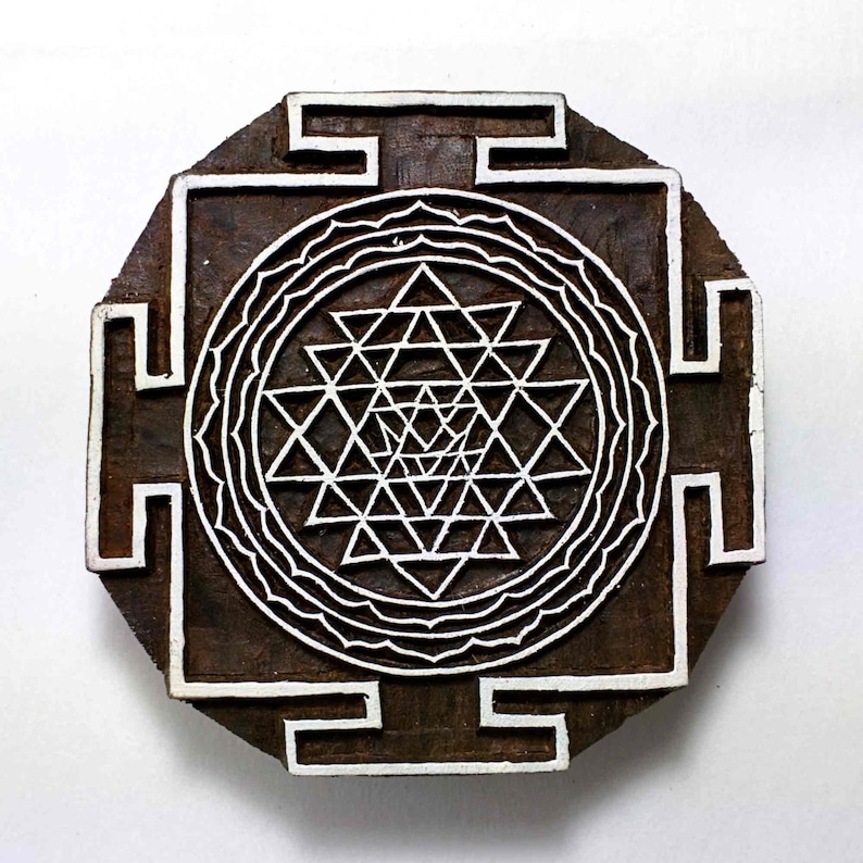 May include: A wooden block printing stamp with a white design of a Sri Yantra, a sacred geometric symbol in Hinduism. The design is surrounded by a square frame with a decorative border.