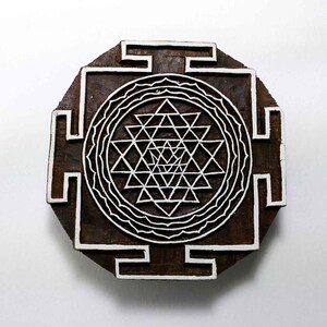 May include: A wooden block printing stamp with a white Sri Yantra design. The design is a geometric pattern of interlocking triangles within a circle.