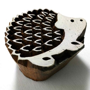 May include: Wooden printing block shaped like a hedgehog with a white design. The block is brown and has a textured surface.