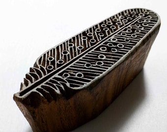 May include: A wooden block printing stamp carved with a detailed feather design. The stamp is brown and has a natural wood grain. It is a traditional Indian craft used for textile printing.