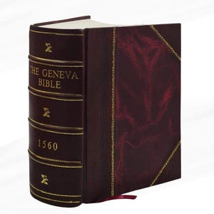 Puede incluir: Un libro encuadernado en cuero burdeos titulado "THE GENEVA BIBLE 1560" con letras y detalles dorados. El libro tiene un borde dorado decorativo y una cinta roja como marcador.