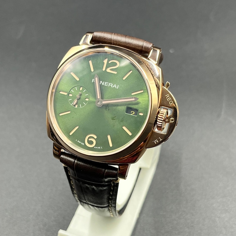Puede incluir: Un reloj de pulsera Panerai con esfera redonda verde, manecillas e &iacute;ndices dorados, ventana de fecha en la posici&oacute;n de las tres y un subdial de segundos. El reloj tiene una caja dorada con protector de corona y una correa de cuero marr&oacute;n.
