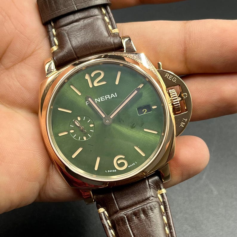 Puede incluir: Un reloj de pulsera Panerai con esfera redonda verde, manecillas e &iacute;ndices dorados. La esfera muestra el texto PANERAI, una ventana de fecha y un peque&ntilde;o subdial de segundos. Tiene una caja dorada con protector de corona marcado REG. T.M.