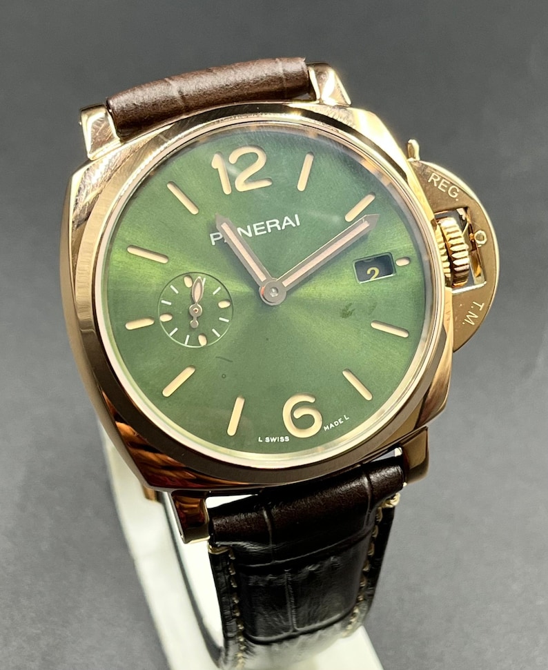 Puede incluir: Un reloj de pulsera Panerai con caja dorada pulida, esfera verde con acabado rayos de sol y correa de cuero marr&oacute;n oscuro. La esfera presenta marcadores de hora dorados, n&uacute;meros ar&aacute;bigos en el 12 y el 6, ventana de fecha en el 3 y segundero en el 9.