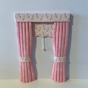 K&ouml;nnte beinhalten: Rosa Stoffvorh&auml;nge mit einer Gardine mit einem wei&szlig;en und blauen Muster aus V&ouml;geln. Die Vorh&auml;nge haben einen wei&szlig;en Besatz mit einer Reihe kleiner rosa Perlen.