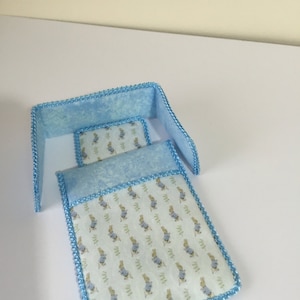 May include: A blue and white miniature doll bed with a Peter Rabbit print on the mattress and a blue and white patterned headboard.