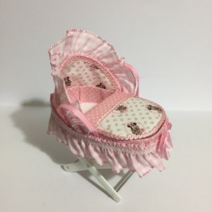 May include: A pink and white baby doll crib with a floral and polka dot pattern and a white wooden base.