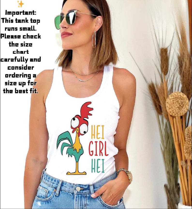 Puede incluir: Camiseta sin mangas blanca con un gr&aacute;fico de gallo de dibujos animados y el texto "HEI GIRL HEI" en rojo, amarillo y verde. La camiseta sin mangas se usa con jeans azules. La imagen tambi&eacute;n incluye texto que dice que la camiseta sin mangas es peque&ntilde;a.