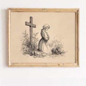 May include: A framed sepia-toned print depicts a person kneeling in prayer before a wooden cross. The person is wearing a long dress and head covering. The cross is behind the person, and there are flowers and grass around the cross and person.