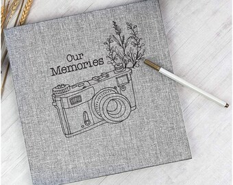 May include: Gray photo album with a camera and floral design. The album cover reads "Our Memories".
