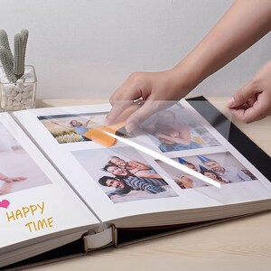 K&ouml;nnte beinhalten: Eine Person bringt eine transparente Plastikfolie auf ein Fotoalbum an. Das Album ist auf einer Seite mit mehreren Fotos einer Familie ge&ouml;ffnet. Auf der Seite steht auch der Text "Happy Time".