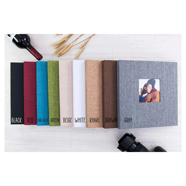 May include: A set of ten photo albums in various colors, including black, red, blue, green, beige, white, khaki, brown, and gray. Each album has a textured fabric cover and a small window for displaying a photo.