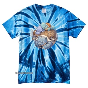 Puede incluir: Camiseta azul teñida con un diseño de tres tortugas de dibujos animados. La tortuga más grande es azul, con dos tortugas más pequeñas sobre su espalda. La camiseta tiene cuello redondo y una etiqueta de algodón.