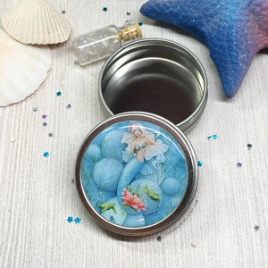 May include: A round metal tin with a mermaid illustration on the lid. The mermaid is blue and green with long white hair and is surrounded by blue and white bubbles. The tin is open and the inside is silver.