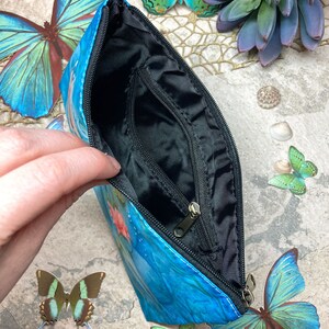 May include: A blue zippered pouch with a butterfly design. The pouch is open and the inside is black.