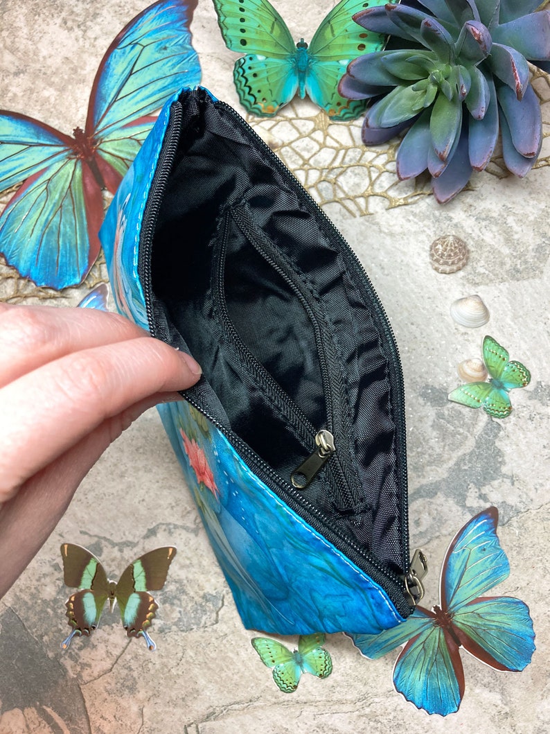 May include: A blue zippered pouch with a butterfly design. The pouch is open and the inside is black.